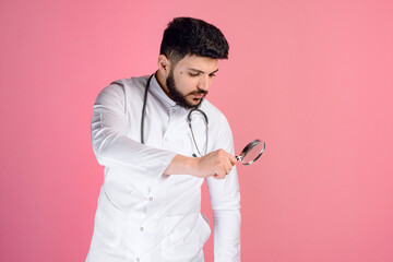 Side view of brunette male doctor, intern, paramedic in uniform standing, holding magnifying glass....