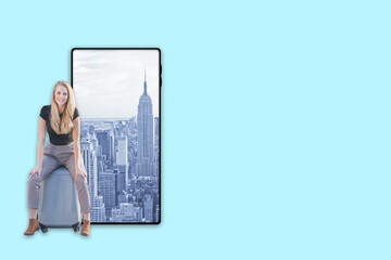 Young smiling woman is sitting on a suitcase near smartphone with Manhattan in the screen. Travel to New York City concept.