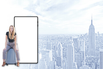 Young smiling woman is sitting on a suitcase near smartphone with blank screen ready for your text. Manhattan is in the background.Travel to New York City concept.