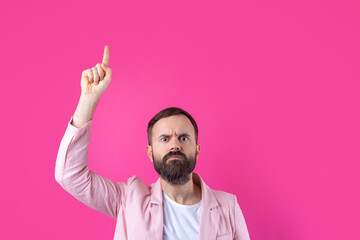 A man dressed in a pink jacket indicates the direction on a pink isolated background.