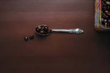 Zelfklevend Fotobehang a silver spoon lies on a wooden surface, there are coffee beans in it, several grains have fallen nearby, top view © Катерина Толстая