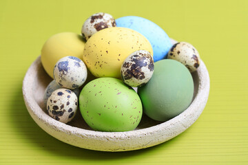 Bowl with Easter eggs on green background.