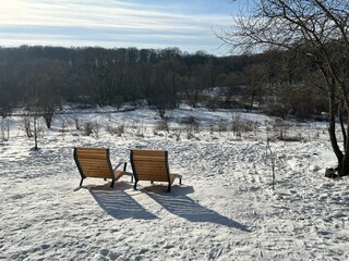 Two comfortable wooden benches, similar to sun loungers, are installed on a raised platform overlooking the winter valley.
