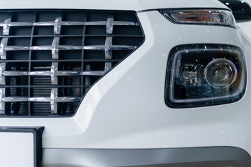 Part of radiator grille and headlights of modern car on white bumper close-up