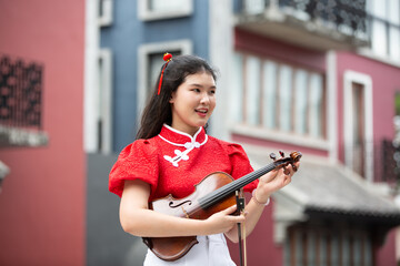 Portrait of Asian young woman play violin with feeling happy and smile in red shirt in city outdoor