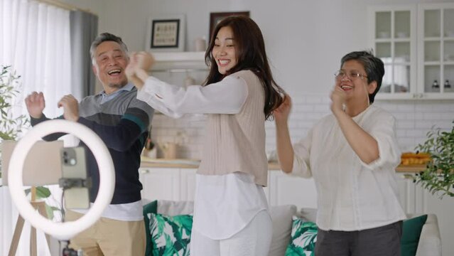 Asian woman using mobile phone take video clip of senior people dancing to share streaming application.Asian senior parent and daughter recording video vlog on social media app in living room at home