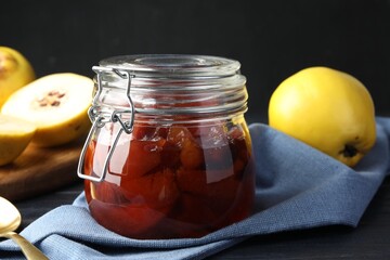 Quince jam in glass jar, spoon and fresh raw fruits on table, closeup