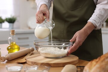 Making bread. Man pouring milk into bowl with flour at wooden table in kitchen, closeup