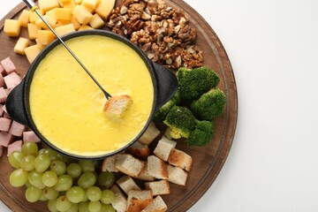 Fondue with tasty melted cheese, fork and different products on white table, top view