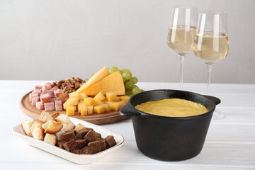 Fondue with tasty melted cheese, different products and aromatic wine in glasses on white wooden...