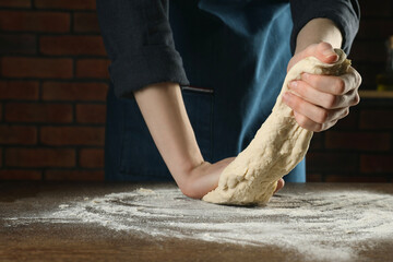 Making bread. Woman kneading dough at wooden table indoors, closeup