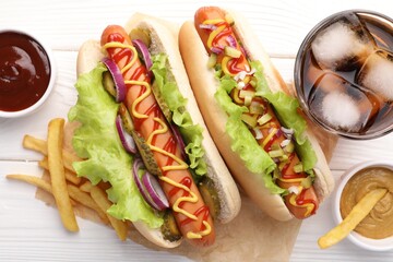 Delicious hot dogs with lettuce, onion and pickle served on white wooden table, flat lay