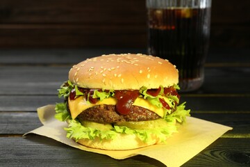 Burger with delicious patty and soda drink on black wooden table