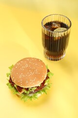 Burger with delicious patty and soda drink on yellow background