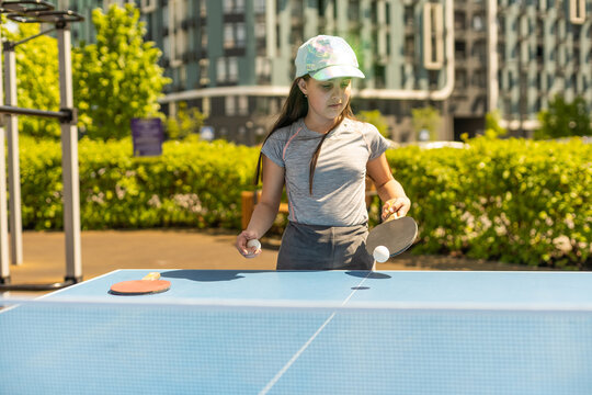 Young teenager girl playing ping pong. She holds a ball and a racket in her hands. Playing table tennis outdoors in the yard
