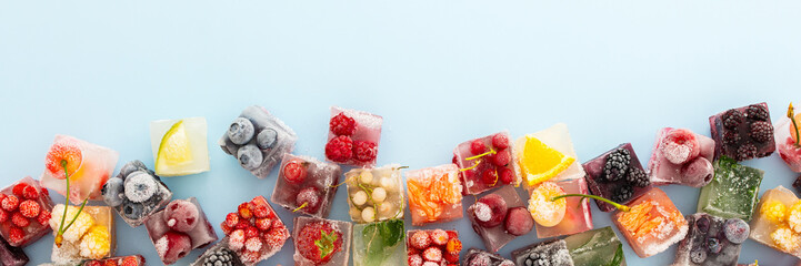 Blue background with ice cubes with frozen berries and fruits and mint, banner