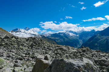 Fototapeta na wymiar Rock formation with panoramic view of majestic snow covered mountain peaks of High Tauern National Park, Carinthia, Austria. Idyllic hiking trail over rocky scree field in summer. Remote Austrian Alps