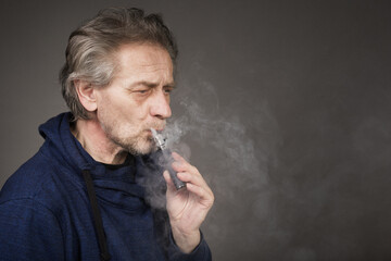 Older man with wrinkles on face skin smoking electronic cigarette