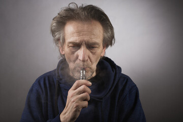 Older man with wrinkles on face skin smoking electronic cigarette