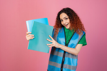 Front view of cheerful lady wearing vest, standing, looking at camera, holsing folders, smiling with open mouth. Concept of aid.