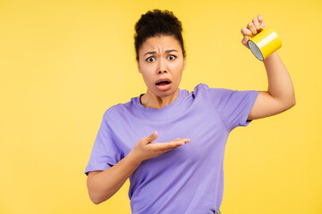 Young African American woman, presenting empty mug with look of astonishment on yellow background