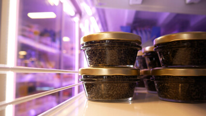 Close-up of many beautiful glass jars of black caviar on a store shelf.