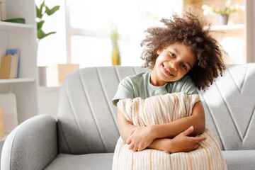 Smiling African American girl perches on a sofa with a pillow in arms