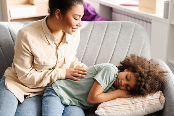 Loving African American mom softly waking her small daughter asleep on the living room sofa