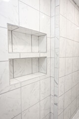 Obraz premium White and gray marbled tile large empty recently renovated home shower in a master bathroom with gold fixtures and a built in tile shelves for bath and body products