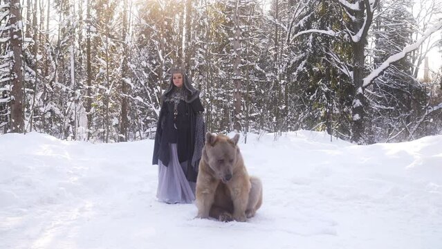 A woman is guiding a bear through the snowcovered forest on a cold winter day