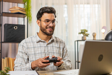Good-looking excited Indian businessman celebrating victory in video game on laptop spending...