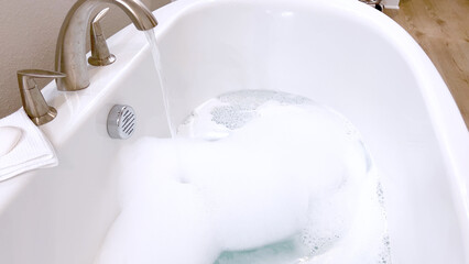 Modern White Bathtub Filled with Running Water from a Brushed Nickel Faucet
