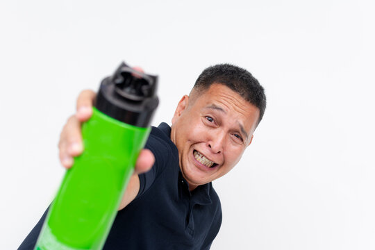A cowardly middle-aged Asian man showing a comical expression of fear while using insecticide spray. Concept of Entomophobia or Katsaridaphobia, or pest problems.