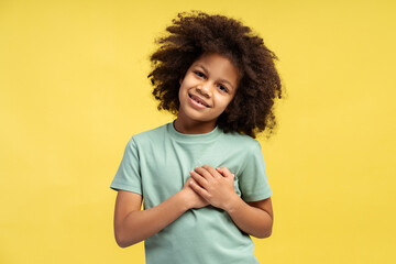 Gleeful little African American girl with curly hair, clasping her hands on her heart in gratitude
