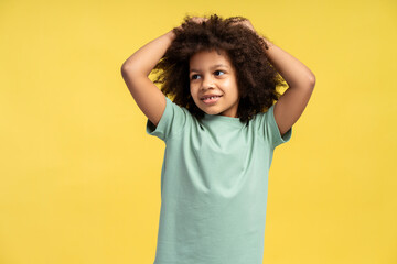 Cheerful African American girl with curls, joyously lifts her hands, isolated on yellow background