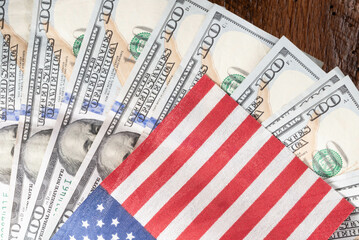 United States currency and flag. One-hundred-dollar bills fanned out on a wooden background.