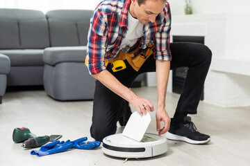 A man is fixing robot vacuum cleaner by hand holding screwdriver to open the cover. Consumables for...