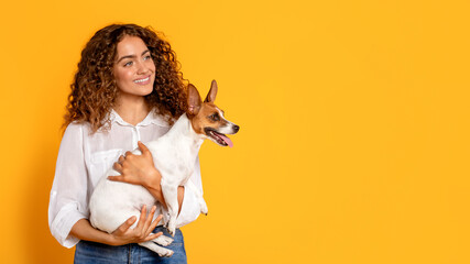 Curly-haired woman lovingly holding Jack Russell Terrier, on yellow background