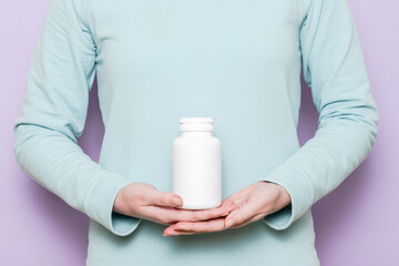 White plastic bottle in female hand. Packaging for pills, capsules or supplements.