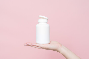 Blank white plastic tube in hand on pink background. Cosmetics beauty mockup for product branding