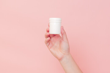 Hand with blank white plastic tube on pink background. Cosmetics beauty mockup for product branding