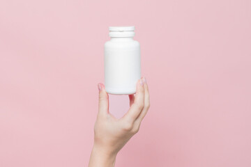 Blank white plastic tube in hand on pink background. Cosmetics beauty mockup for product branding