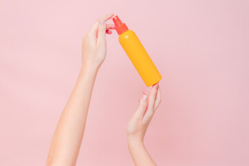 Hand holding plastic spray bottle (as mineral spray or hair spray) on pink background. Cosmetics...