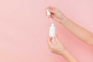 Hand holding glass cosmetic bottle for serum (hyaluronic acid and collagen) on pink background. Beauty concept