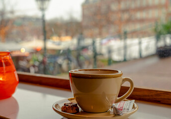Cup of coffee on a table in front of a street with a city view in the background.