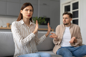 Spouses in heated argument at home, sitting on sofa