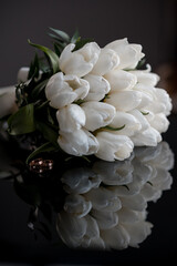 Wedding bouquet of tulips on a black mirror table with wedding rings