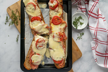 Baked baguette sandwich with italian ham, mozzarella cheese, tomatoes and thyme on rustic bread