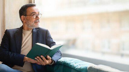 Mature man in glasses engrossed in a book, thoughtful expression