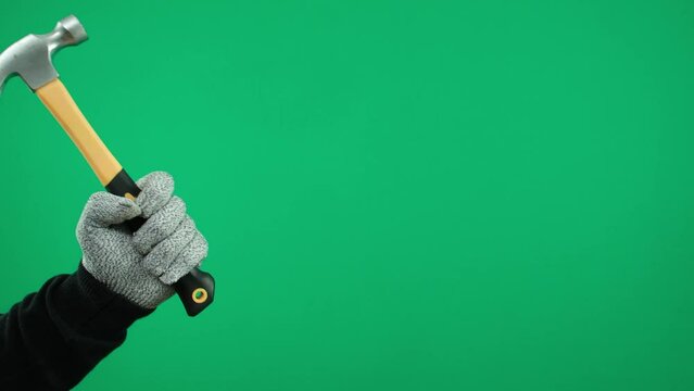 A man's hand in gray gloves holds a hammer on a green background